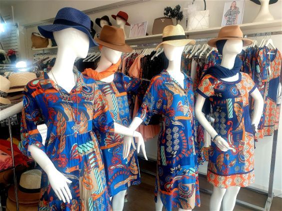 Mannequins wearing colorful dresses and hats in a retail store.