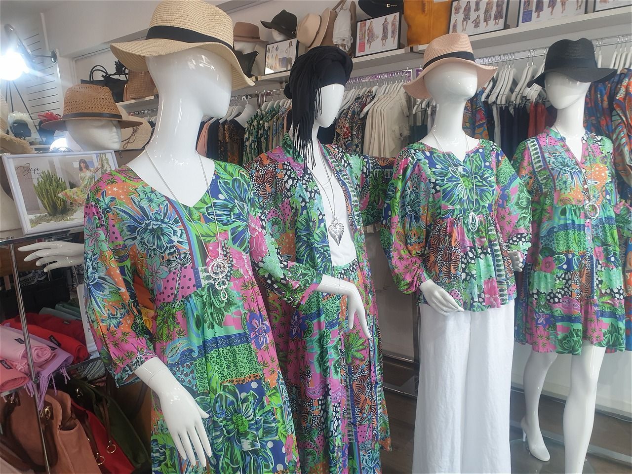 Mannequins in a boutique displaying colorful floral outfits, with hats and white pants.