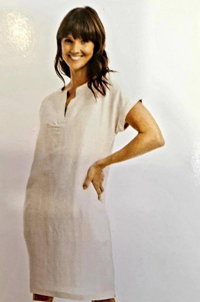Woman in a light-colored linen dress, smiling, with hand on hip.