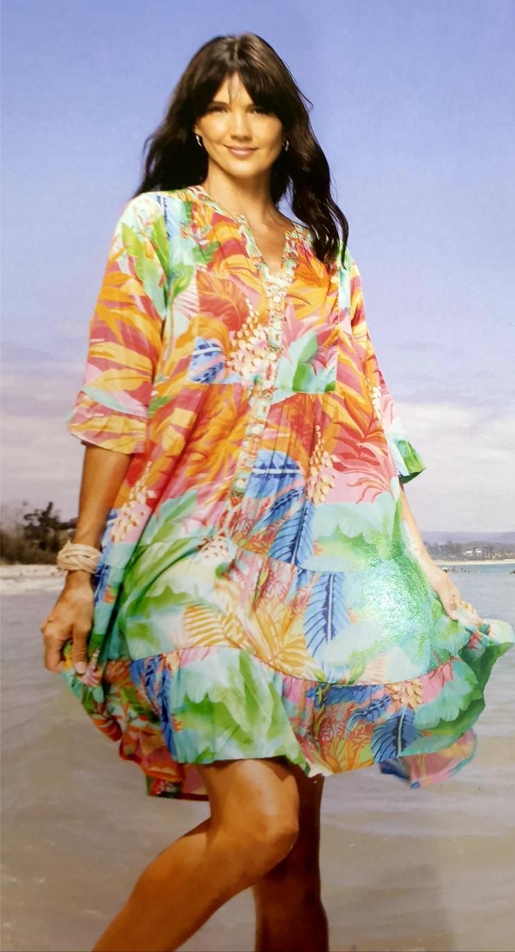 Woman in a colorful floral tunic dress on a beach, smiling.