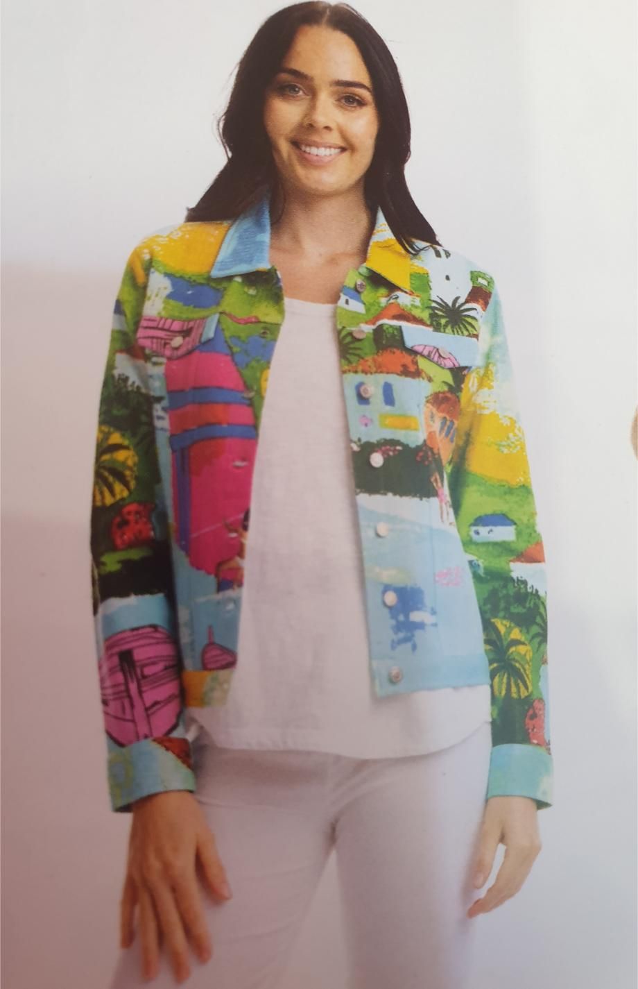 Woman wearing a colorful, painted denim jacket and white outfit; smiling.