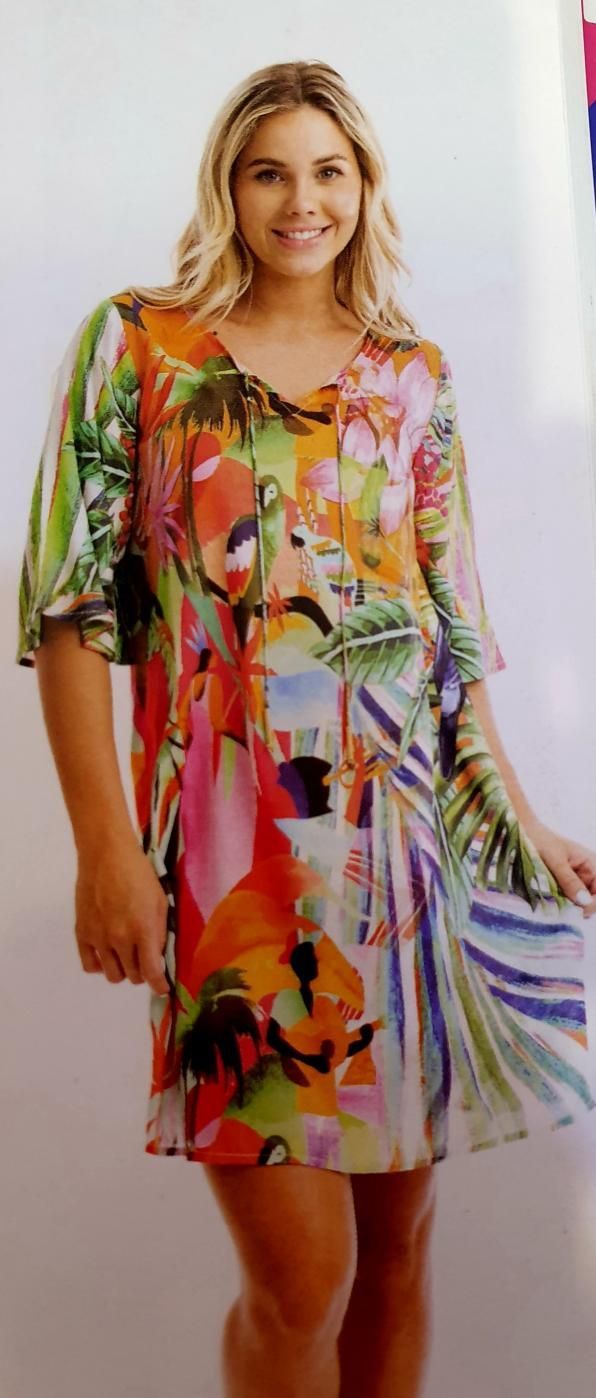 Blonde woman in a colorful, patterned dress smiles, posing indoors.