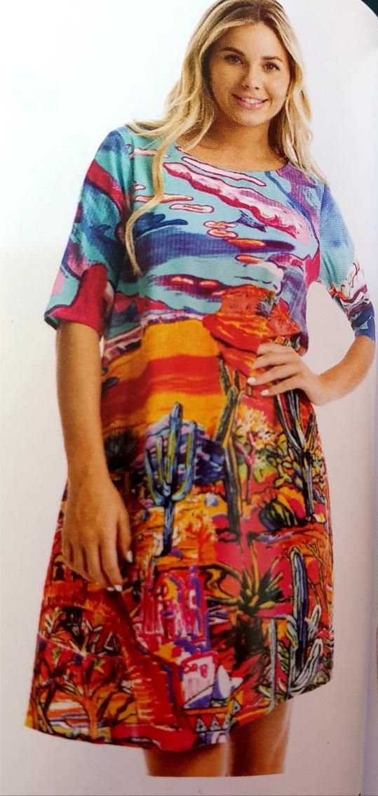 Woman in a colorful dress with a desert landscape pattern, posing with her hand on her hip.