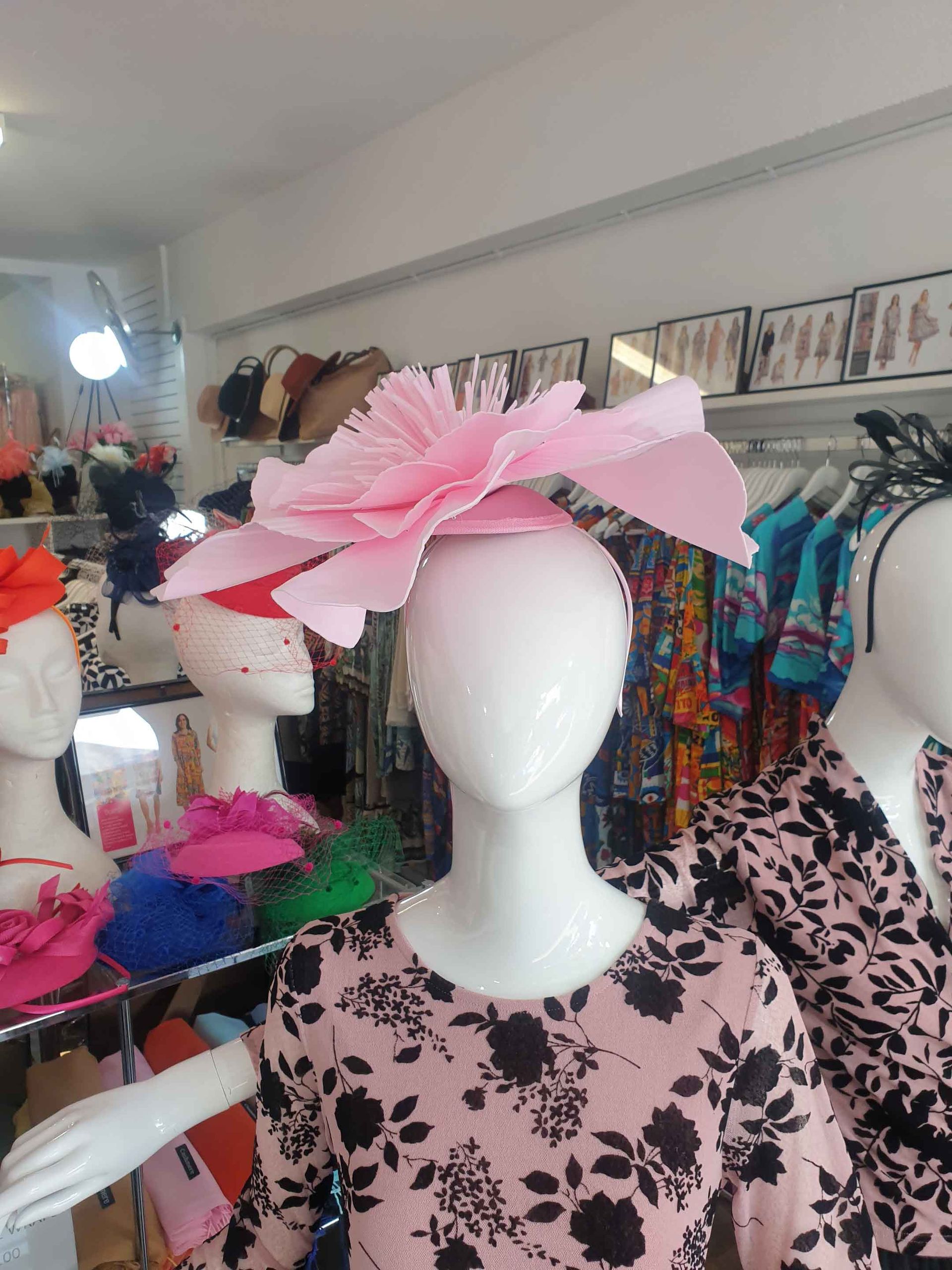 Mannequin wearing a large pink flower hat, displayed in a clothing store.