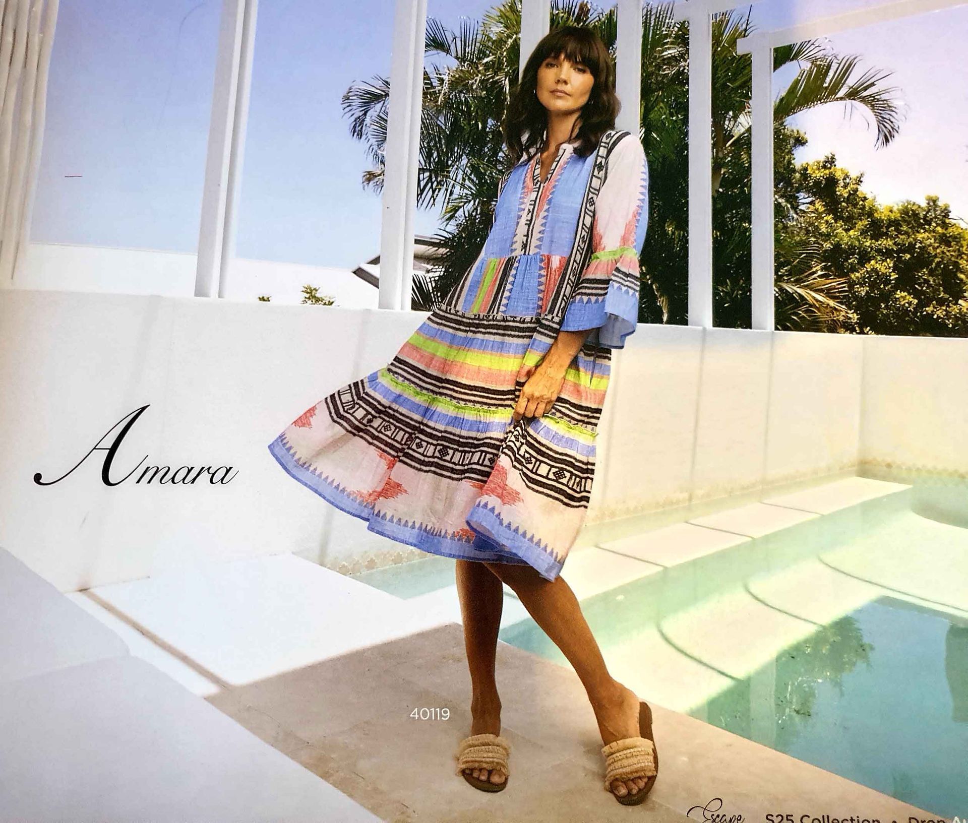Woman in colorful print dress, posing by pool.