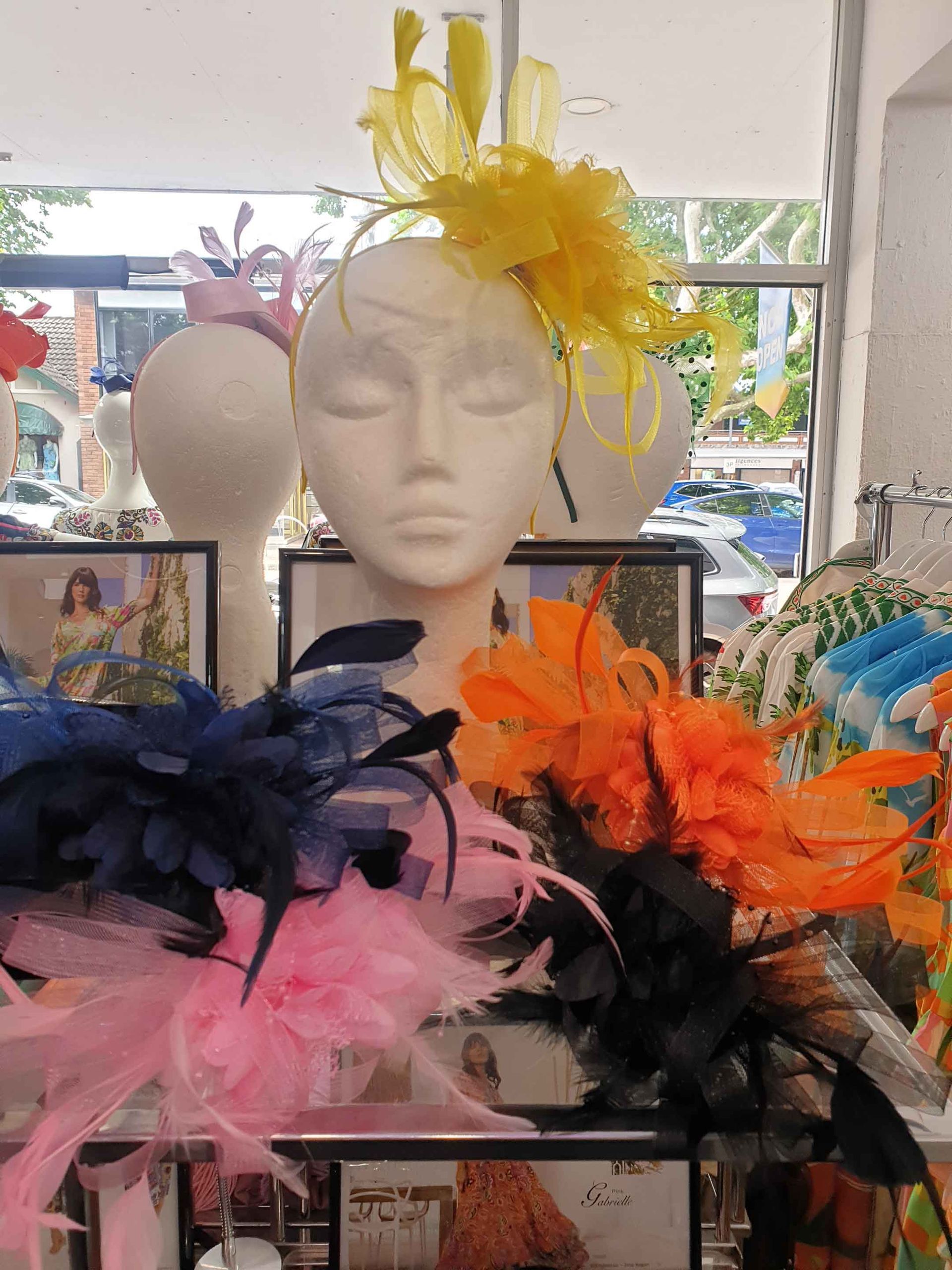 Mannequin head with yellow hat, surrounded by colorful feathered headpieces in a store display.