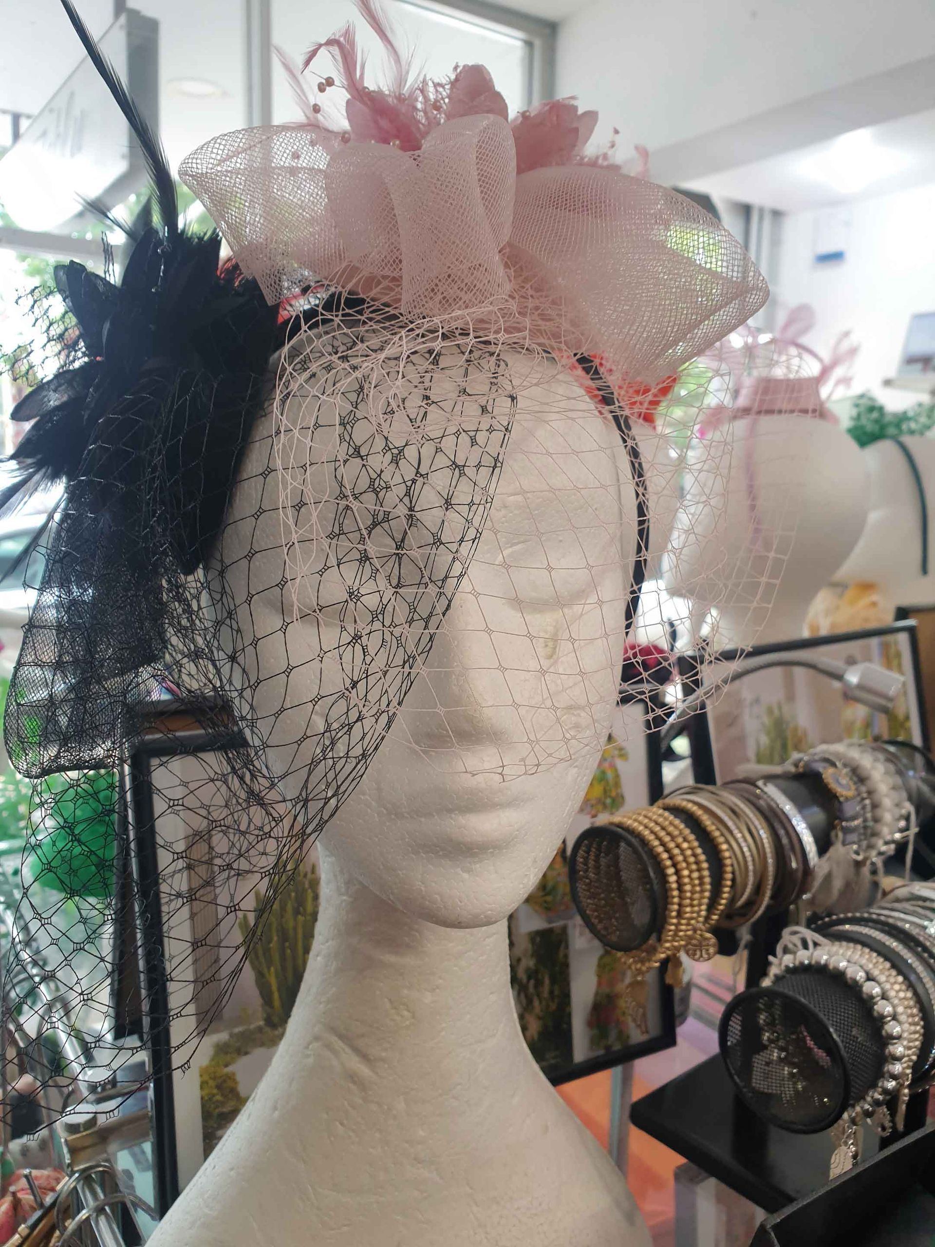 Head mannequin wearing a black and pink feathered fascinator with veil; displayed in a store setting.