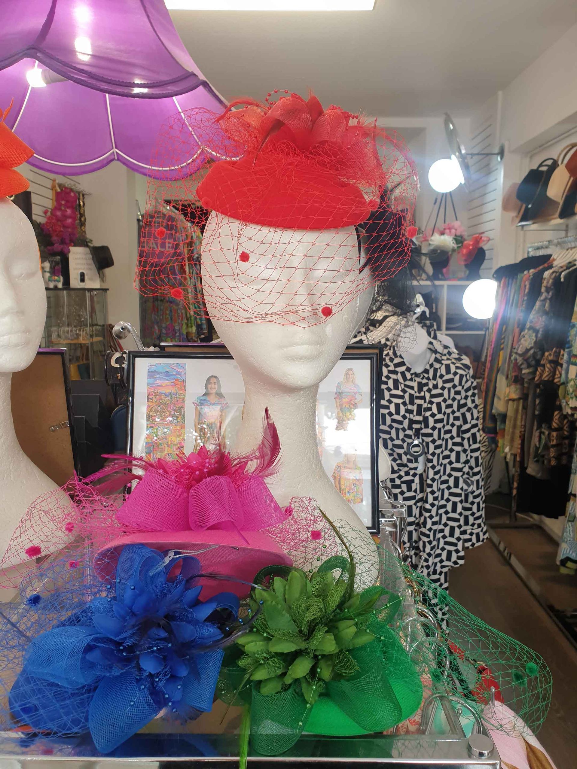 Display of colorful hats on mannequins in a shop. Red, pink, blue, and green hats with veils and embellishments.