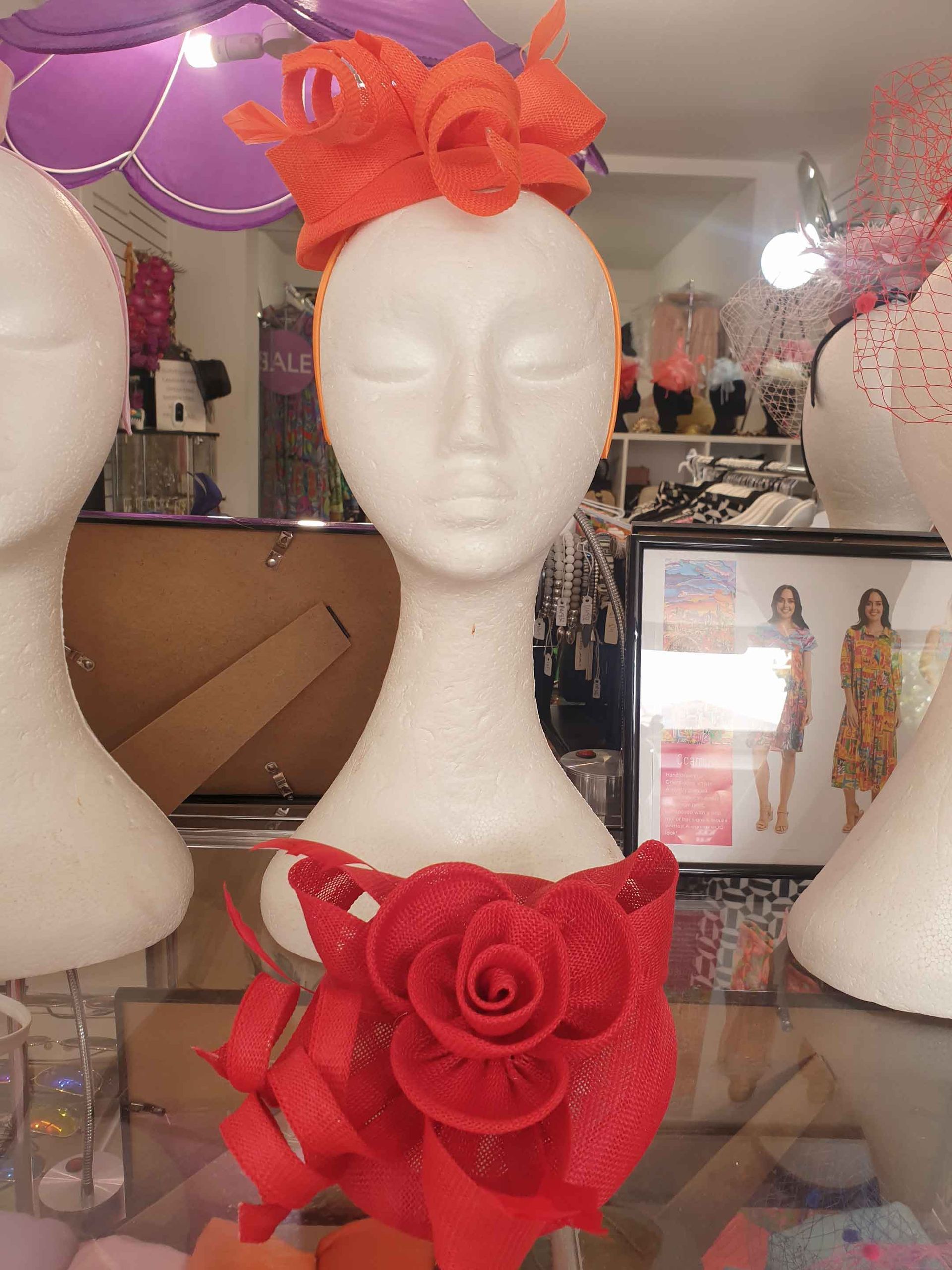 White mannequin head wearing a coral headpiece and a red rose-shaped clutch in a store display.