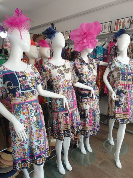 Mannequins in floral dresses, wearing hats, inside a brightly lit clothing store.
