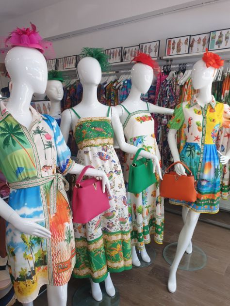 Mannequins in colorful tropical dresses with matching hats and bags in a store.