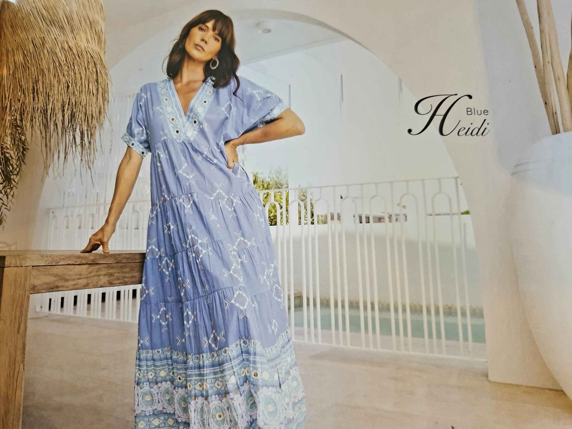 Woman in a light blue patterned maxi dress, standing on a balcony.