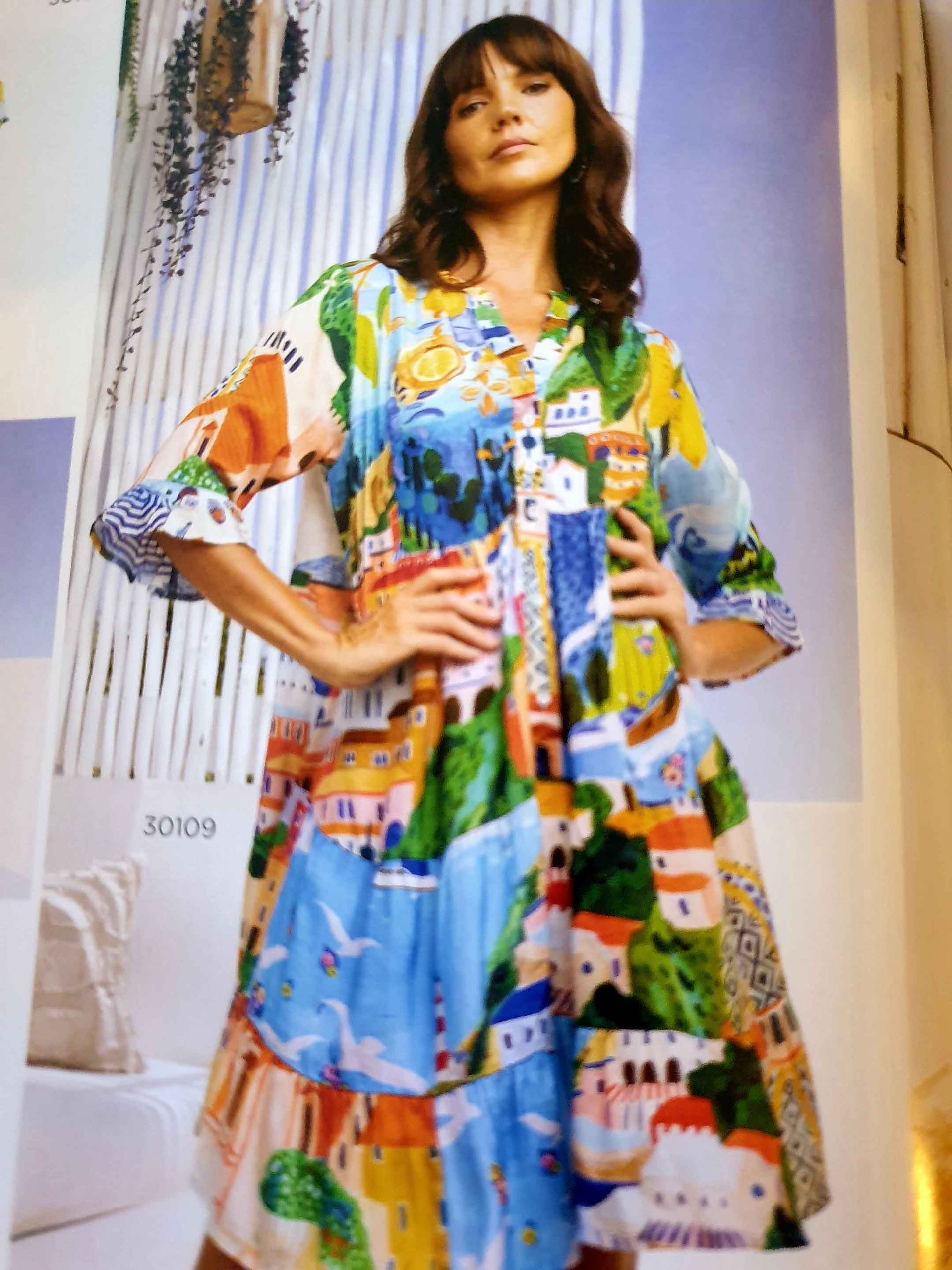 Woman in colorful dress with a village print, arms akimbo.