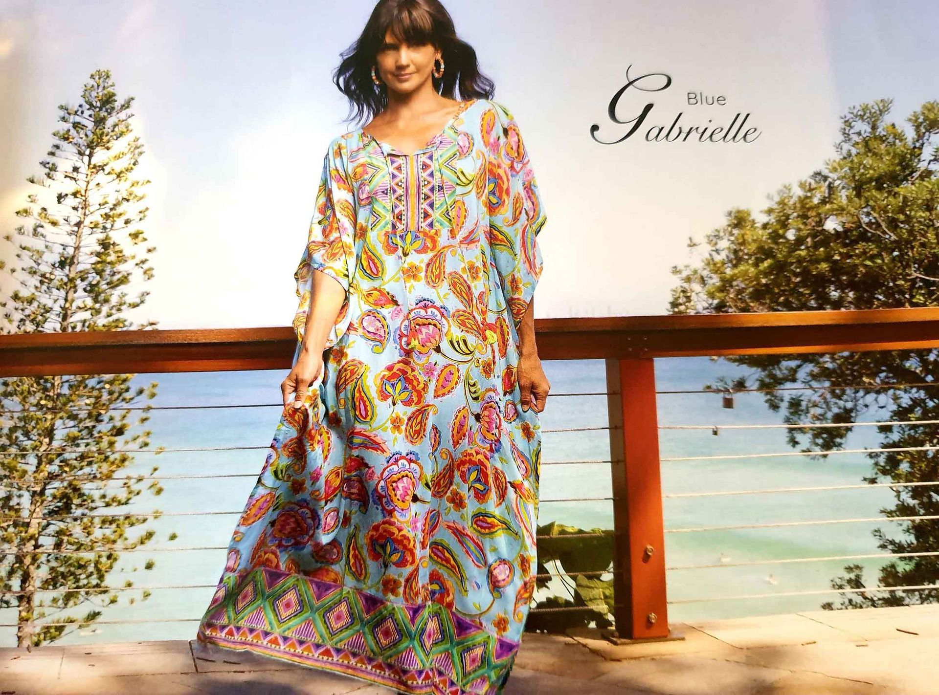 Woman wearing a flowing paisley print dress on a balcony overlooking the ocean.