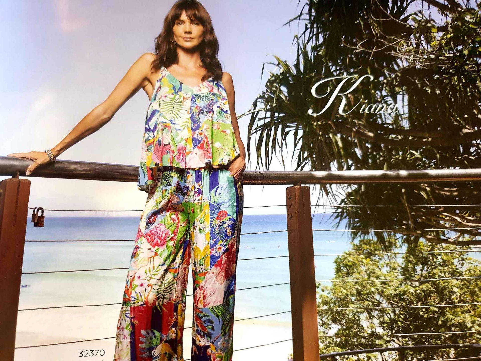 Woman in colorful print outfit on a deck overlooking the ocean; brand logo 