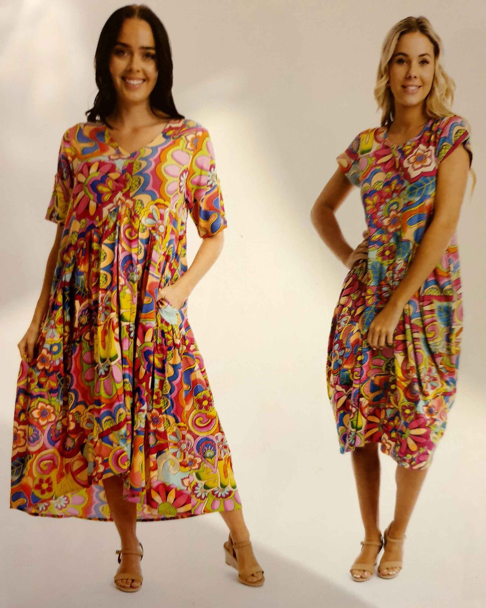 Two women wearing colorful floral dresses. One has short sleeves, the other has a pocket and a cap sleeve. Both are smiling.