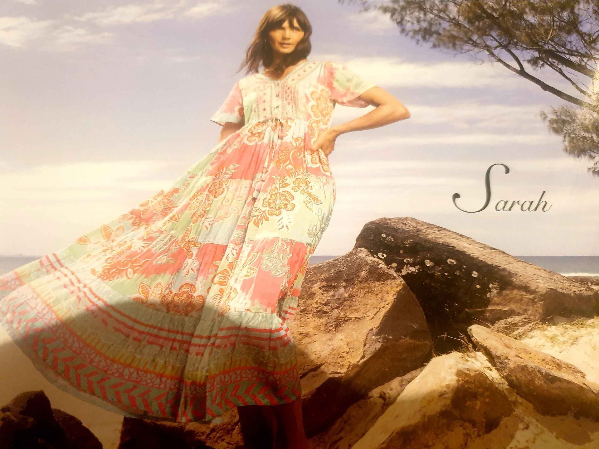 Woman in floral dress poses on rocks by the beach; 