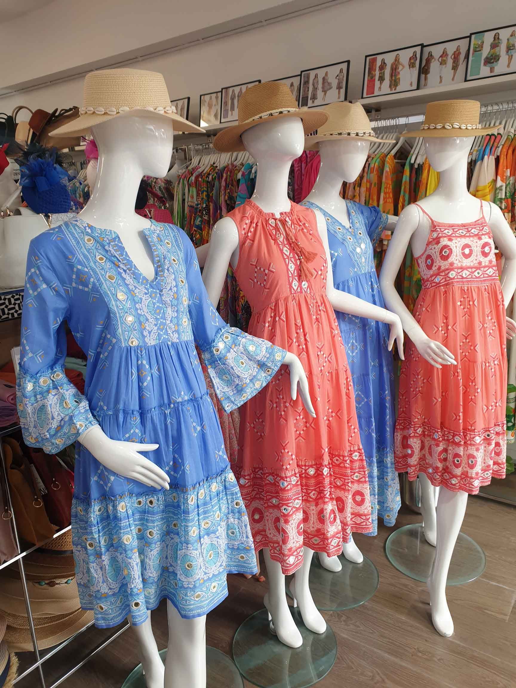 Five mannequins wearing colorful summer dresses and straw hats in a clothing store.