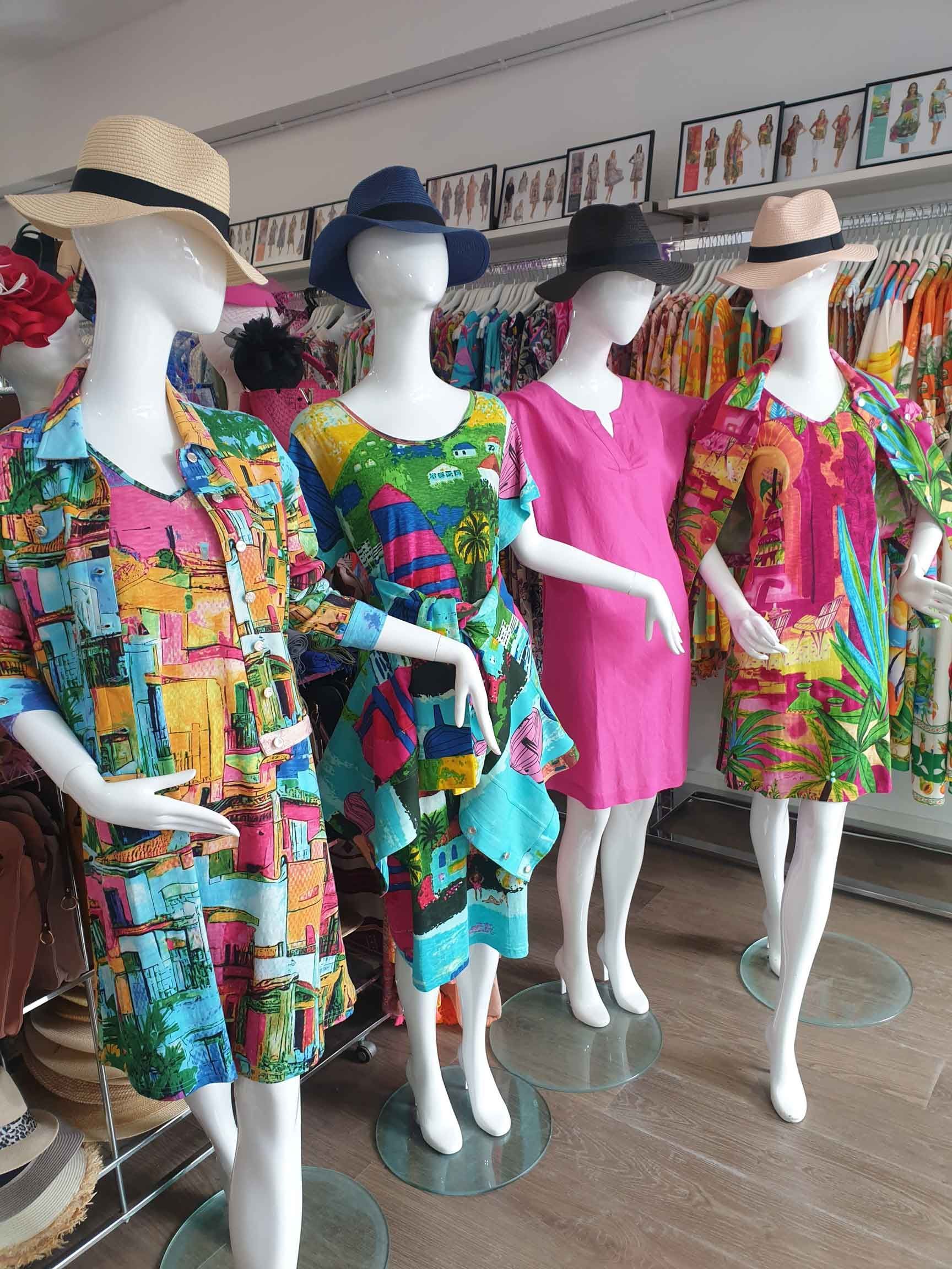Four mannequins wearing colorful dresses and hats in a clothing store.