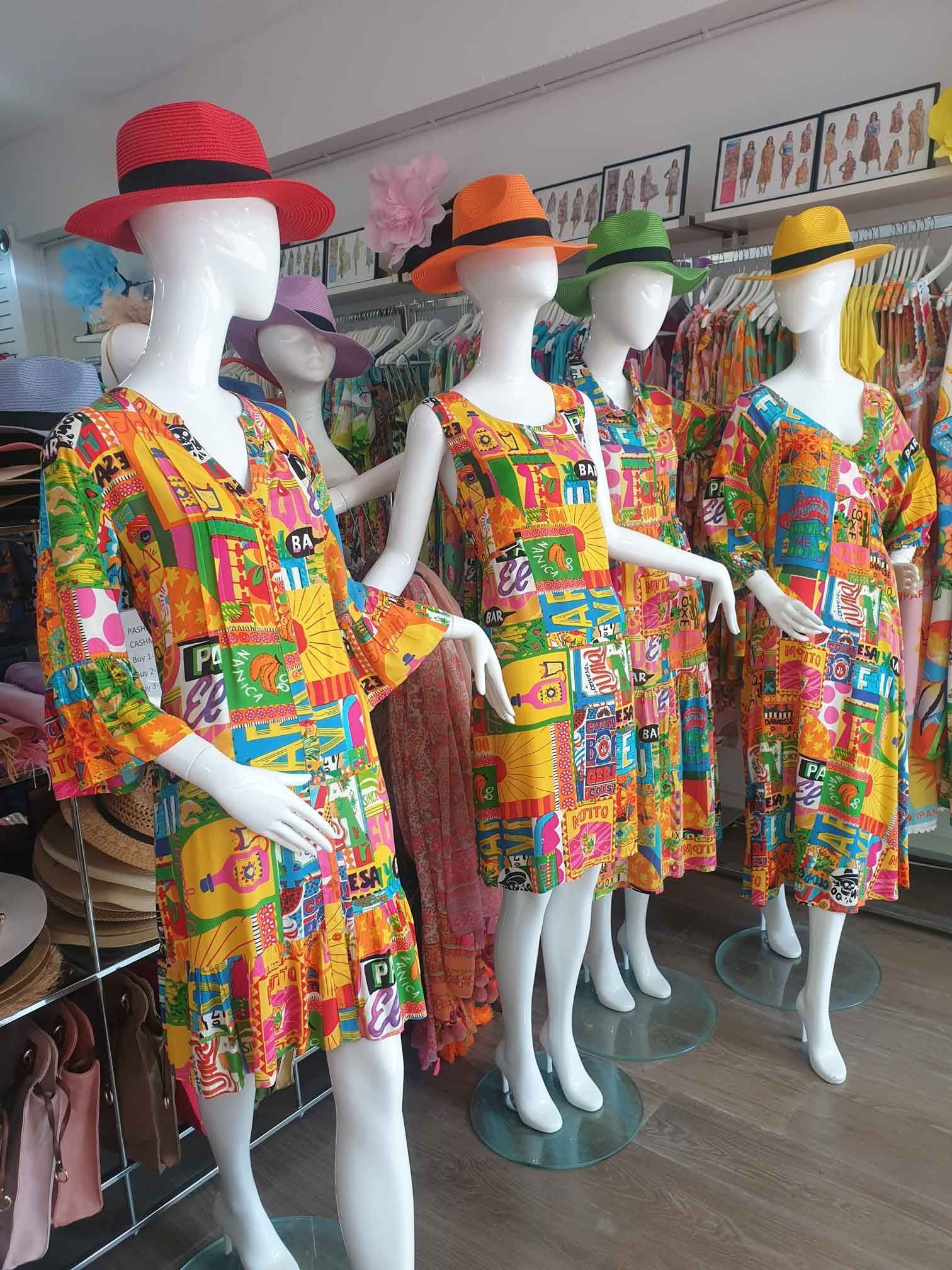Five mannequins in colorful dresses and hats in a store. The dresses are patterned with bright colors, the hats match the colors.
