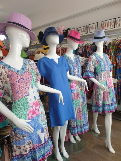 Four mannequins wearing dresses and hats in a clothing store.