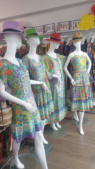 Four mannequins wearing floral dresses and hats inside a store.