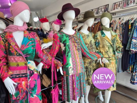 Mannequins in a vintage clothing store, wearing brightly colored dresses and coats, with hats. 