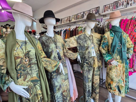Four mannequins in a shop window display wearing green and yellow patterned outfits, all with hats.