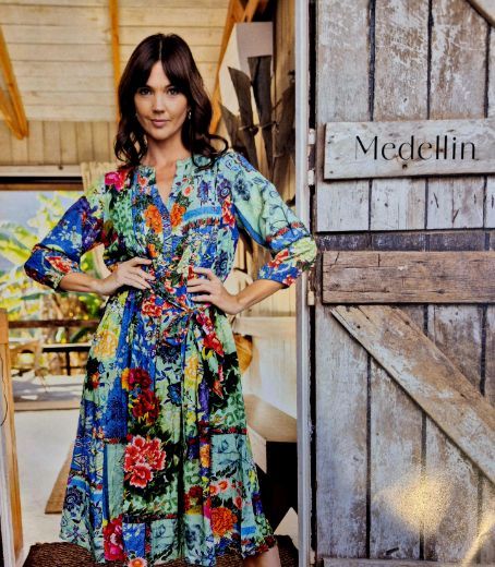 Woman in colorful floral dress stands by a wooden door labeled 