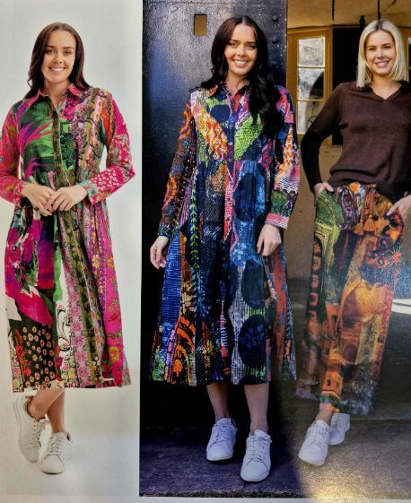 Three women in colorful patterned outfits, smiling. Middle woman in long dress. Side woman with matching pants. All wearing sneakers.