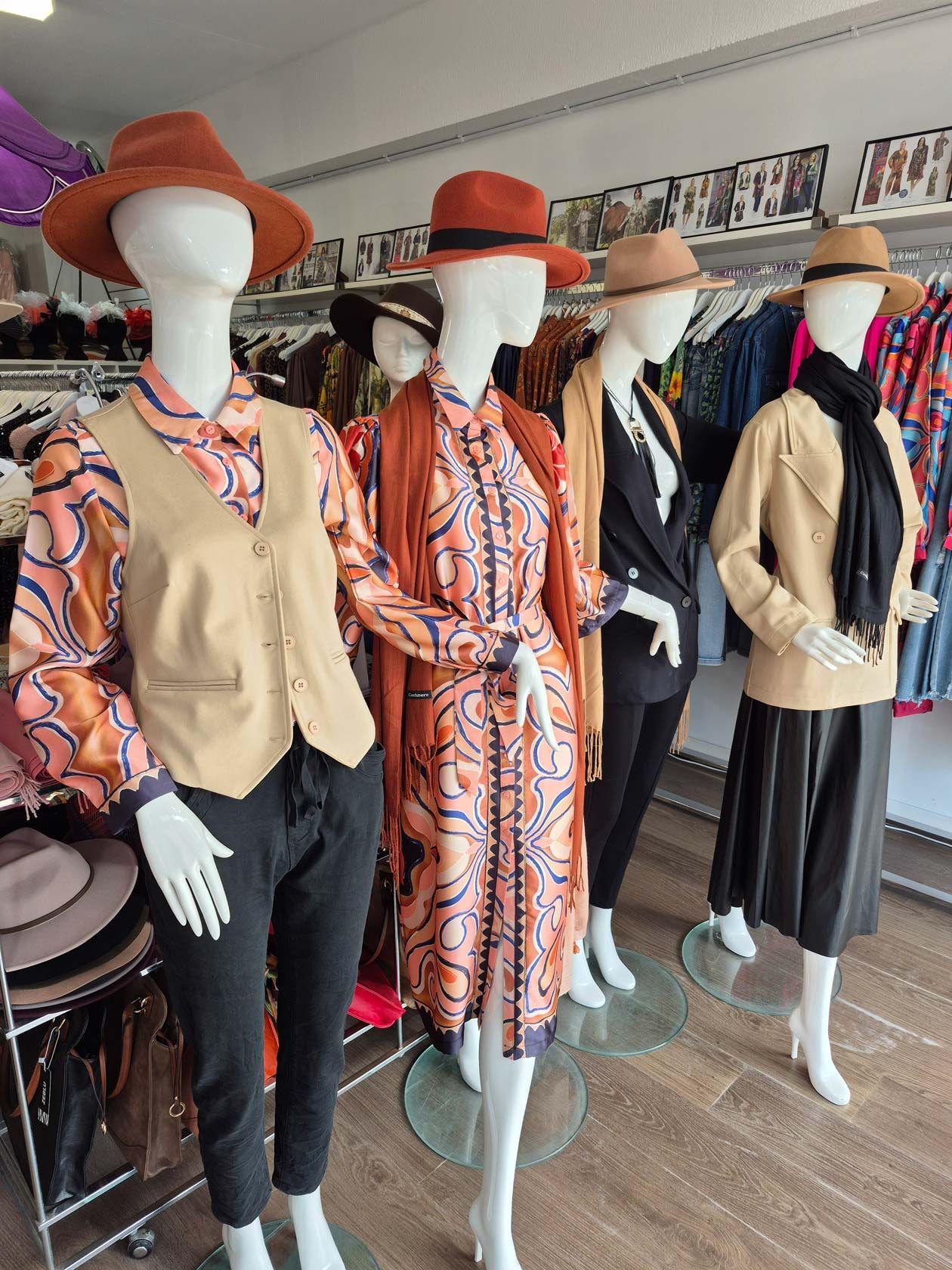 Five mannequins wearing fall clothing, including hats and dresses, in a clothing store.