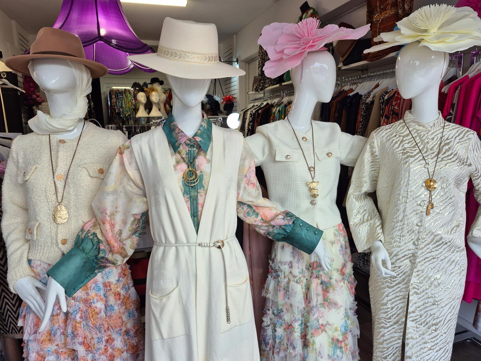 Four mannequins in a shop window display, wearing vintage outfits and hats.