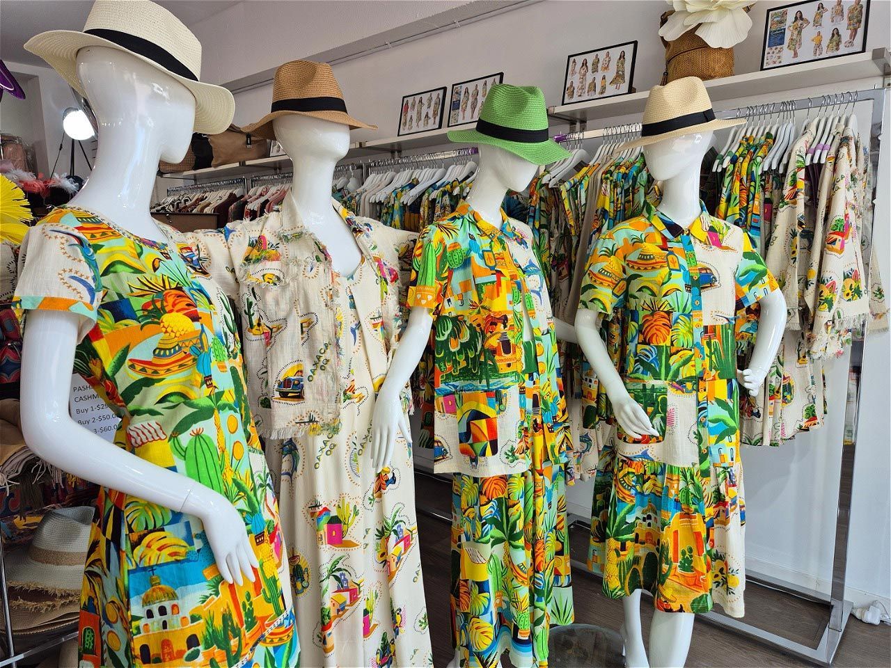 Mannequins wearing colorful summer dresses and hats in a clothing store.