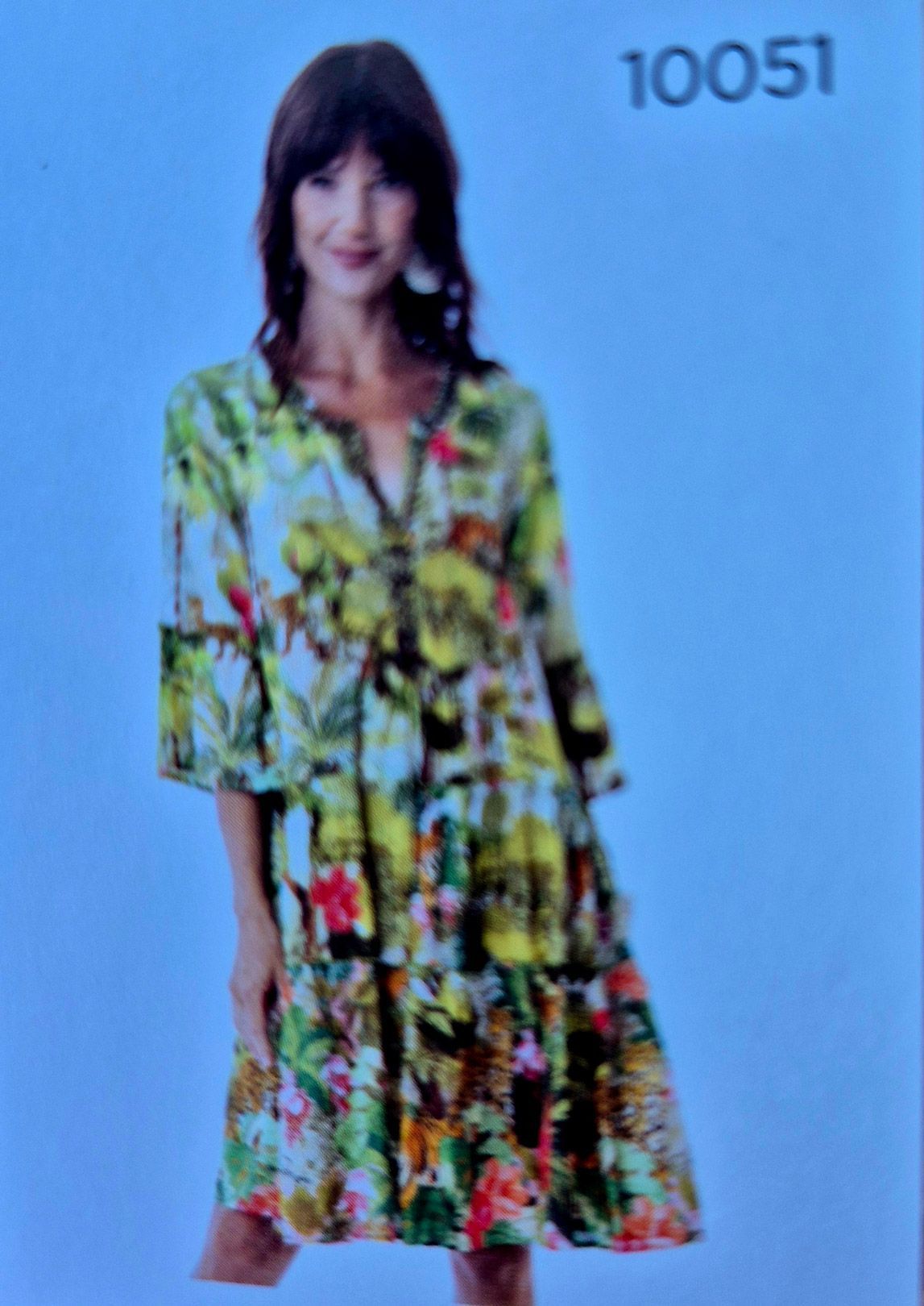 Woman in colorful floral dress with tiered skirt, standing against a blue background.