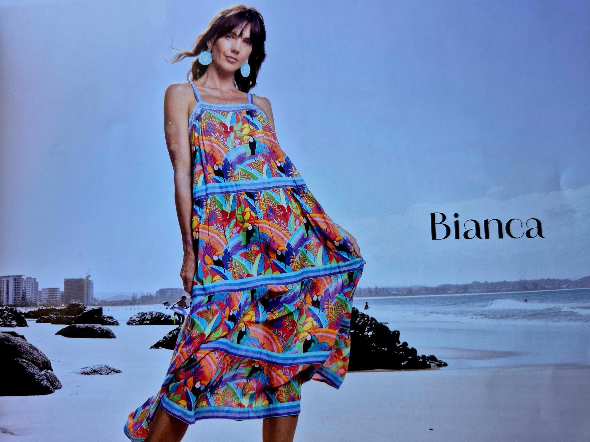 Woman in colorful patterned dress stands on a beach.