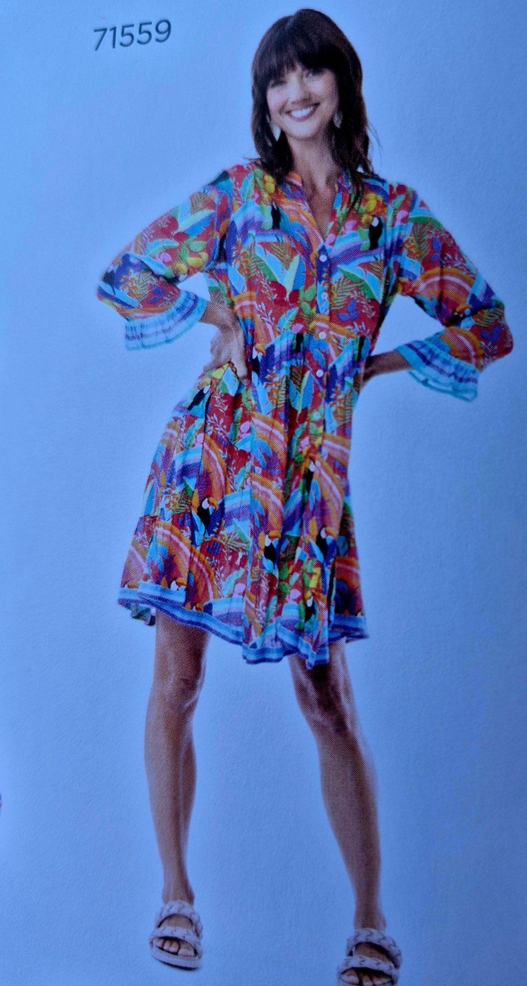 Woman in colorful print dress, hands on hips, smiling.