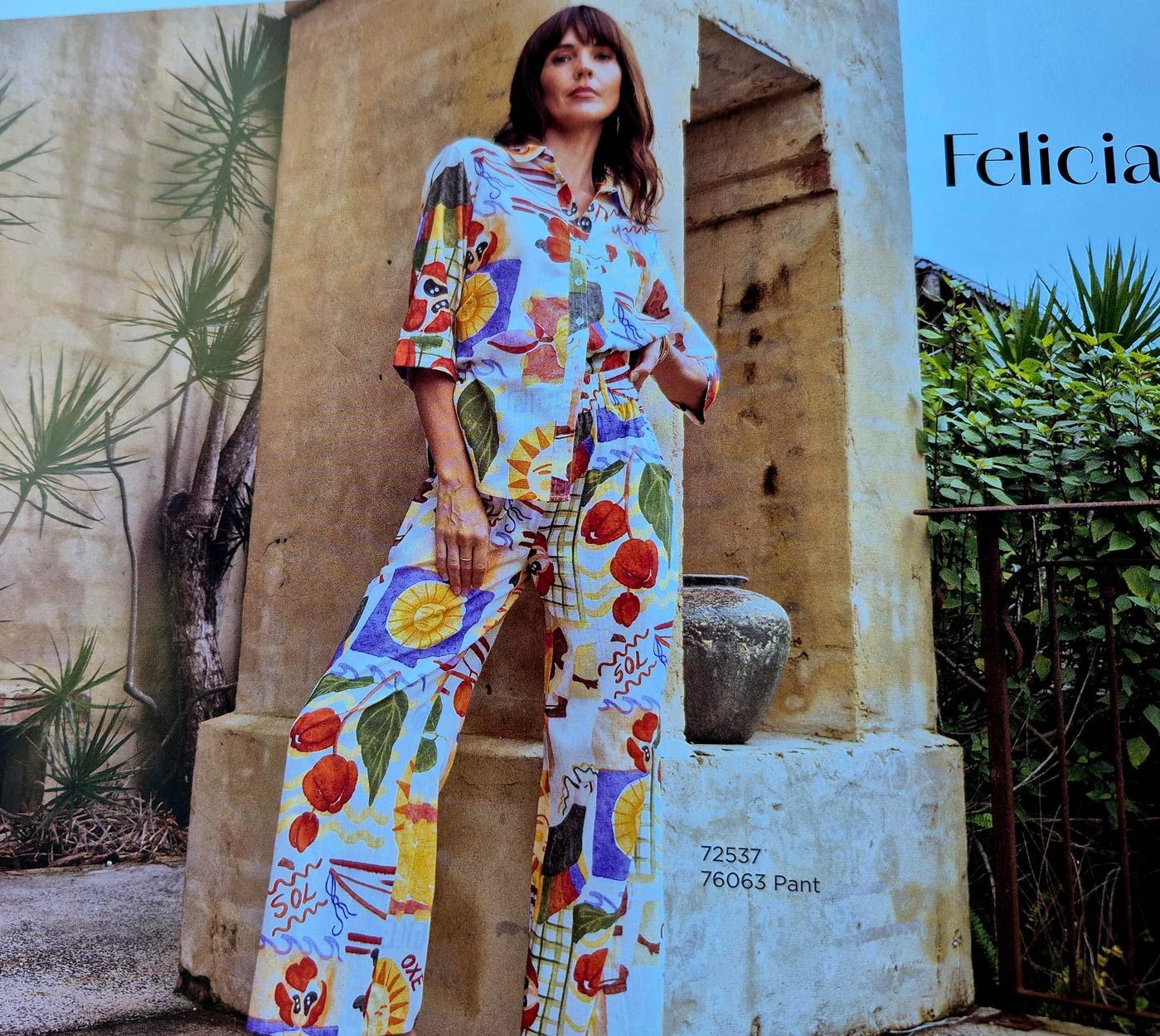 Woman in colorful patterned outfit posing by stone structure.