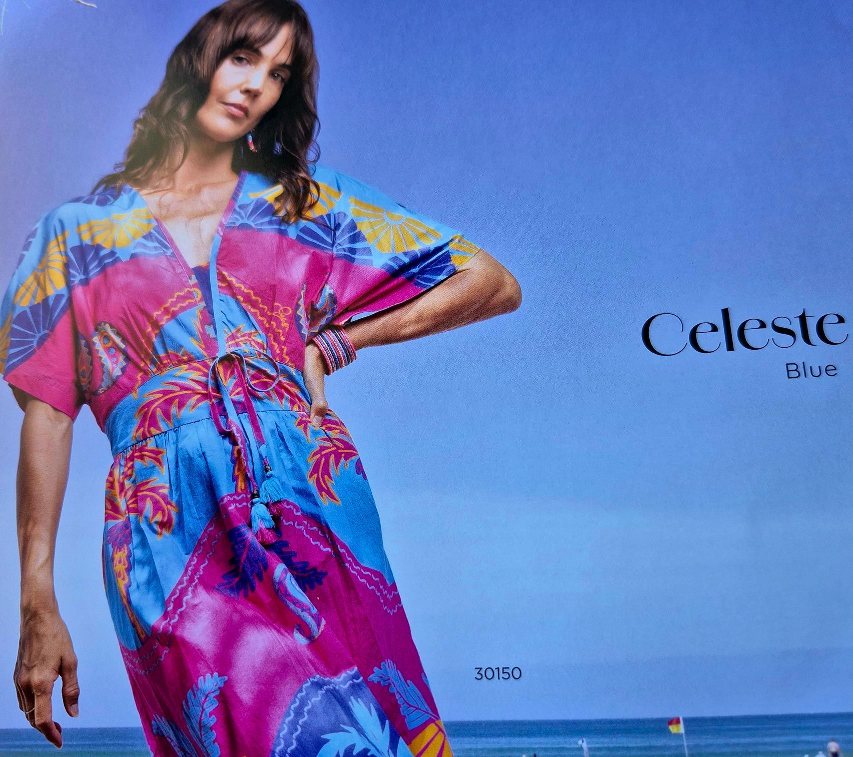 Woman in colorful floral dress, blue sky, beach background.