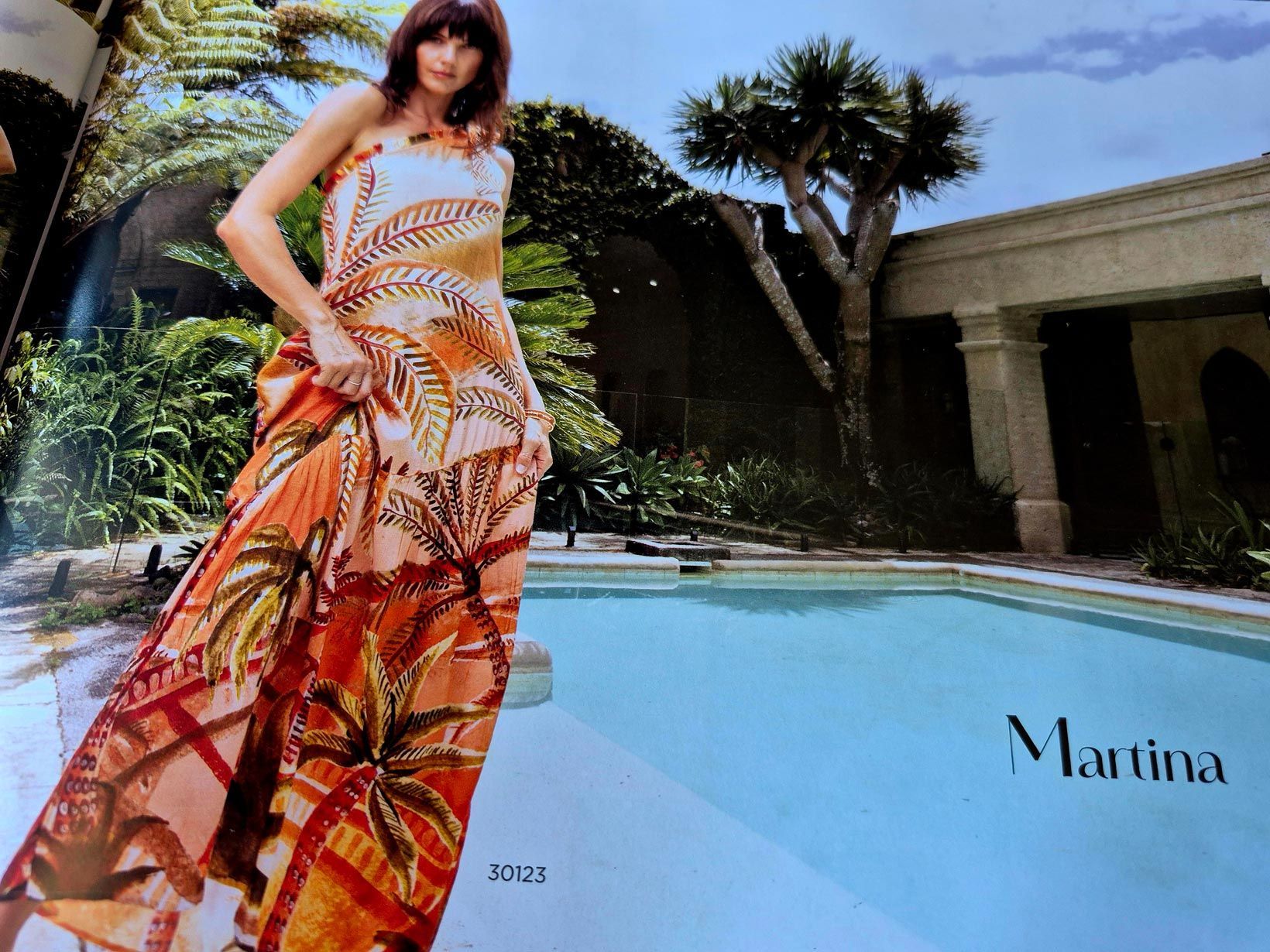 Woman in a tropical print dress stands by a pool.