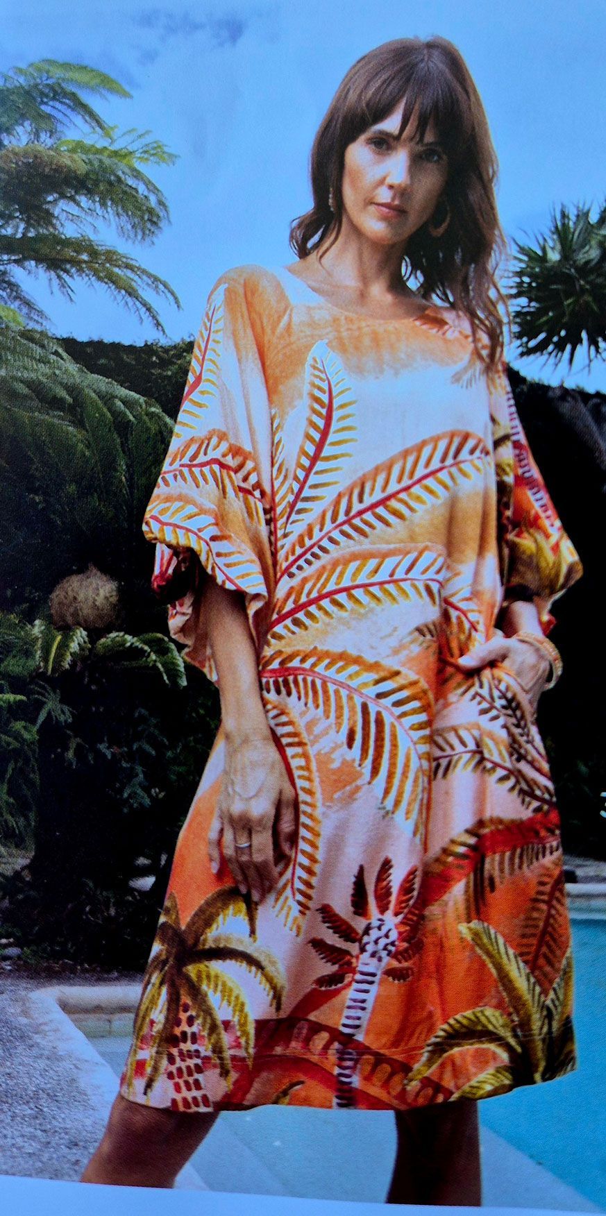 Woman wearing a tropical print dress, standing near a pool.
