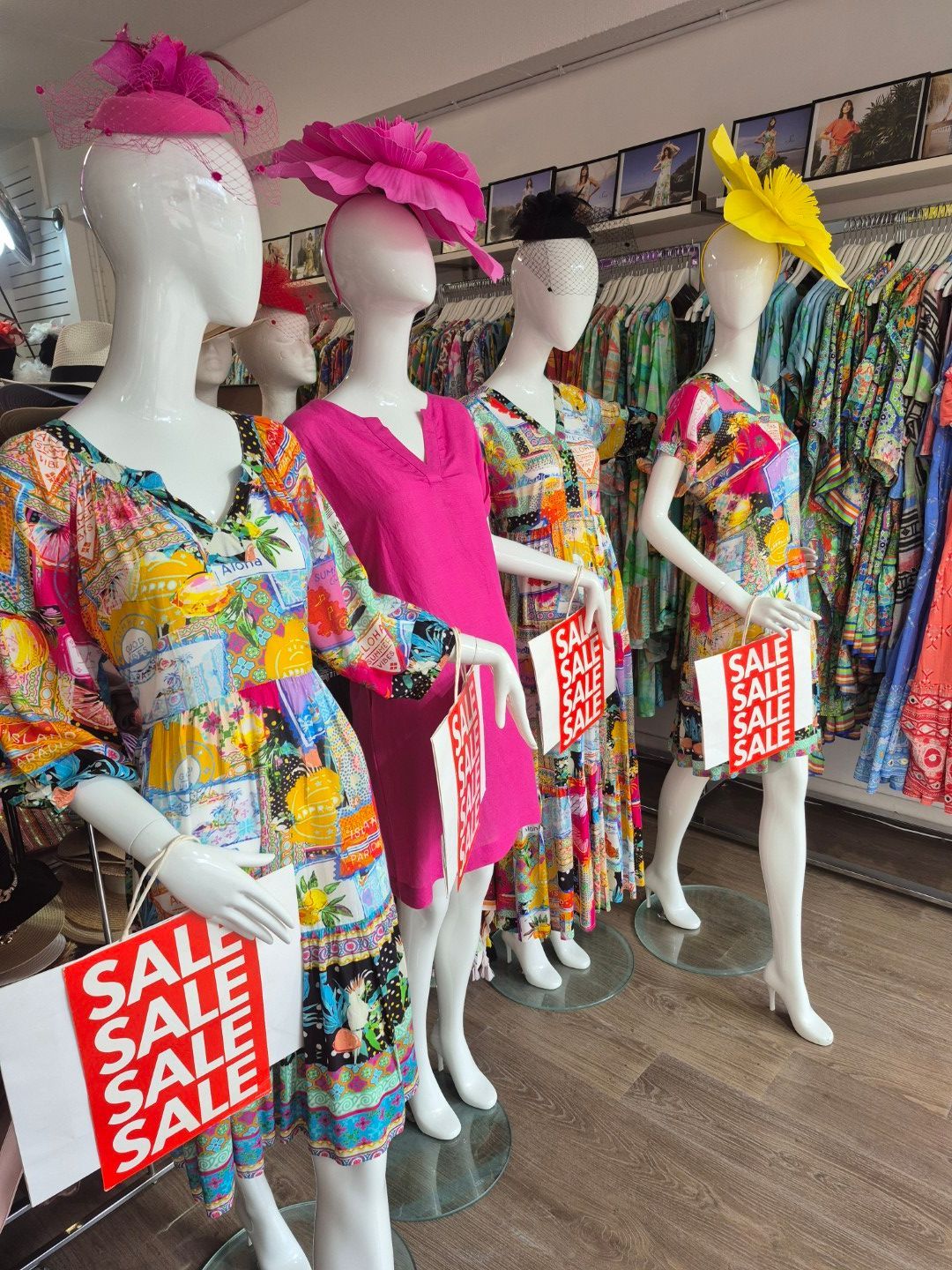 Store mannequins in colorful dresses and hats, each holding a sale sign.