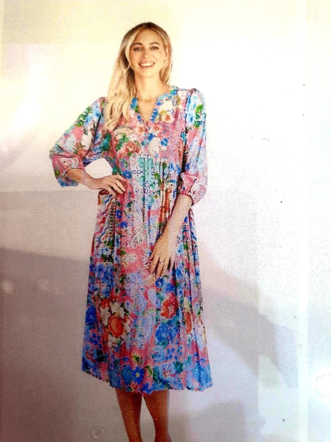 Woman in floral dress smiles, hand on hip.