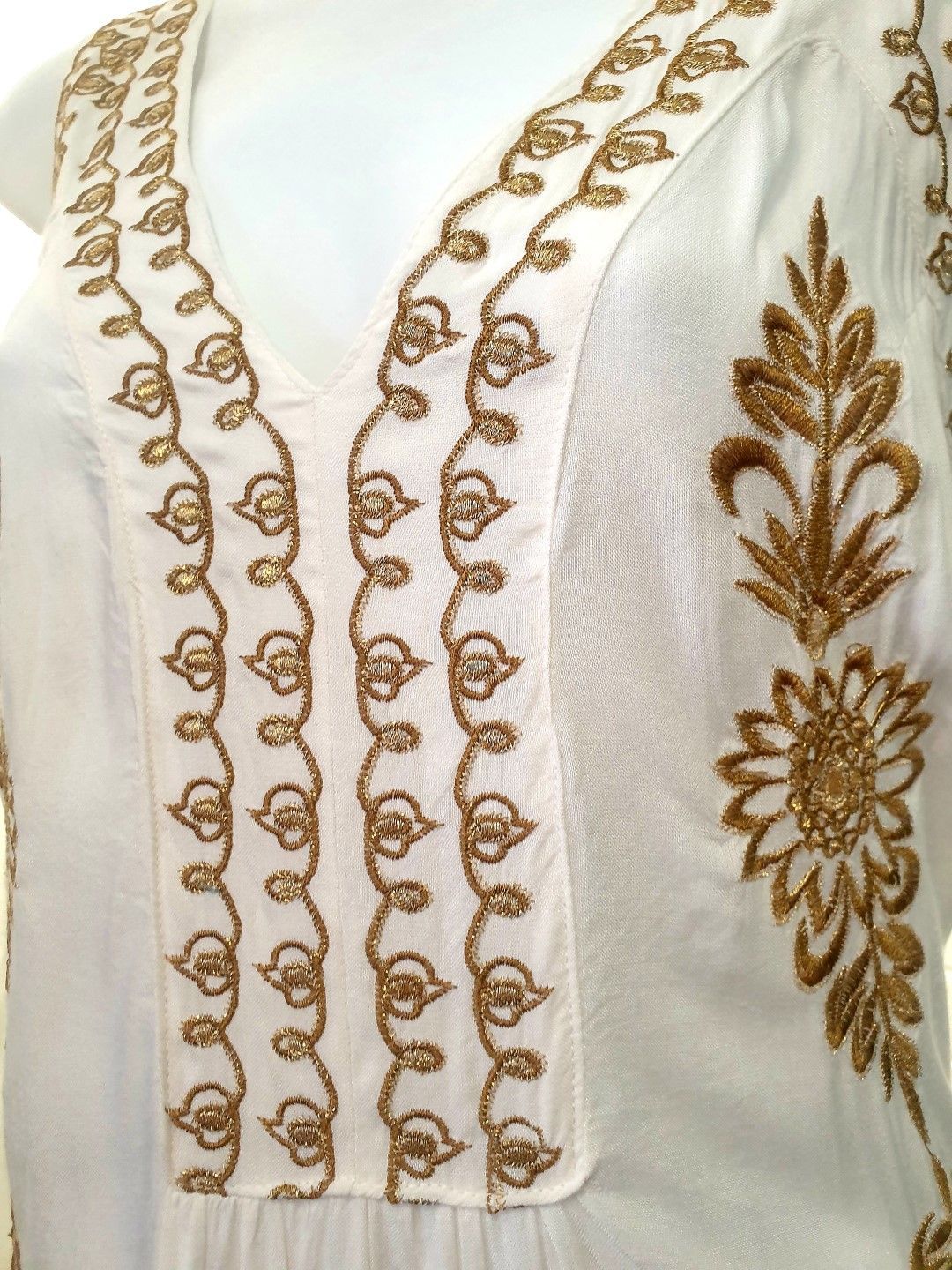 White dress with gold embroidery around the neckline and floral design on the side.