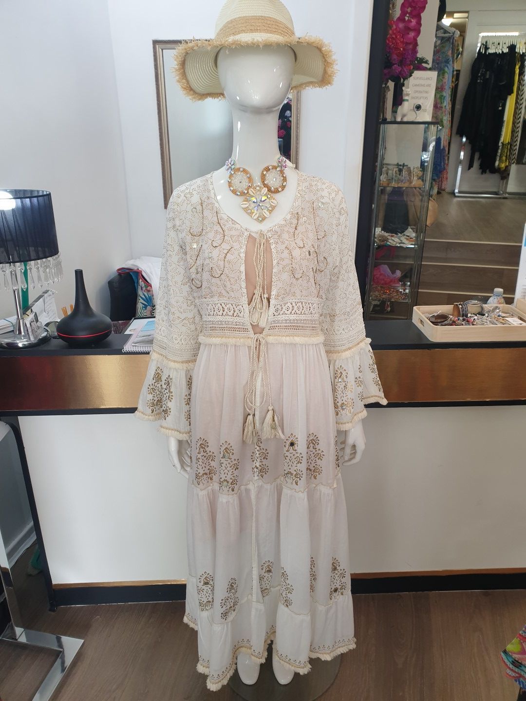 Mannequin in a white dress with a straw hat and gold embellishments. Interior store setting.