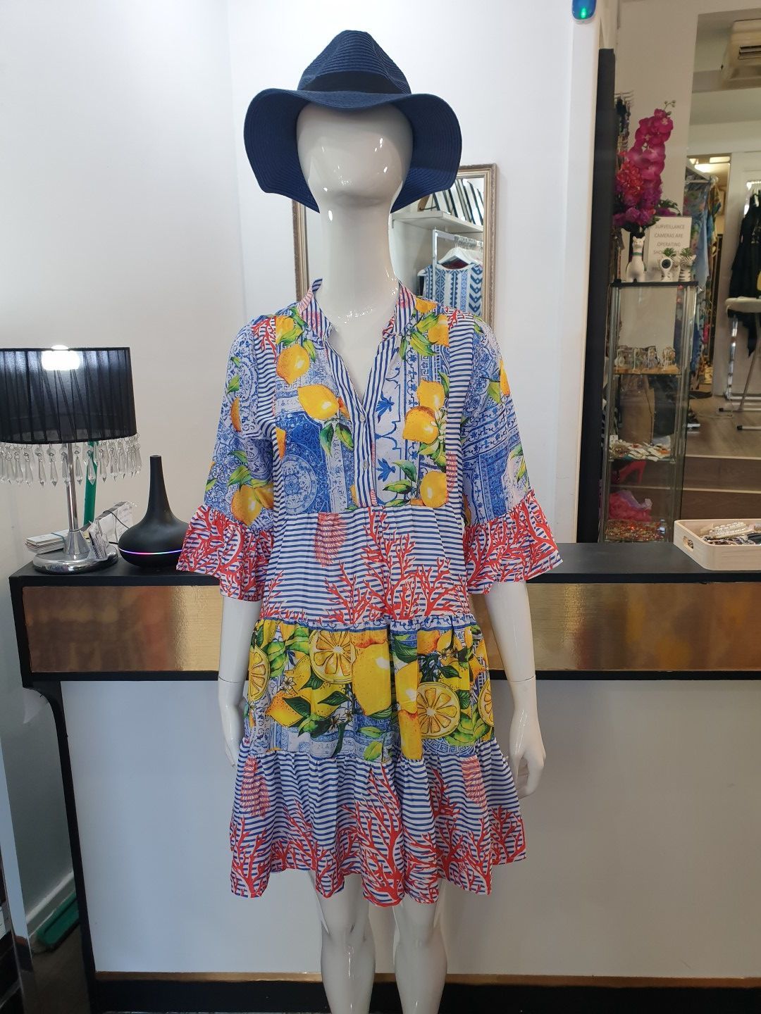 Mannequin in a colorful floral print dress, blue hat. Indoors, display in a boutique.