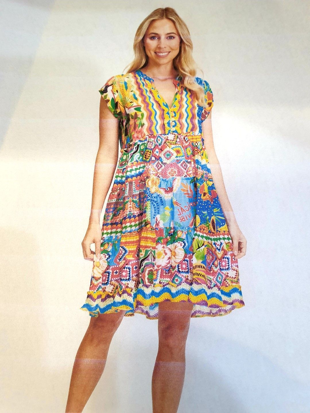 Woman wearing a colorful printed dress smiles, standing in front of a white background.