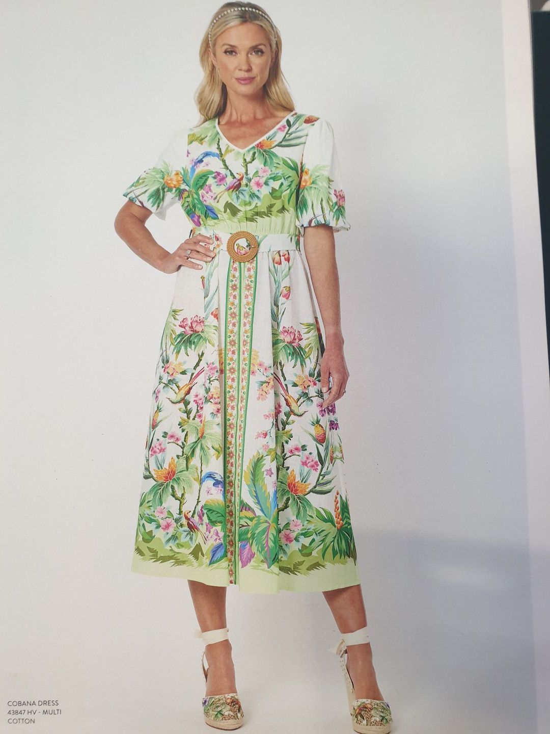 Woman in tropical print dress, belted, posing, white background.