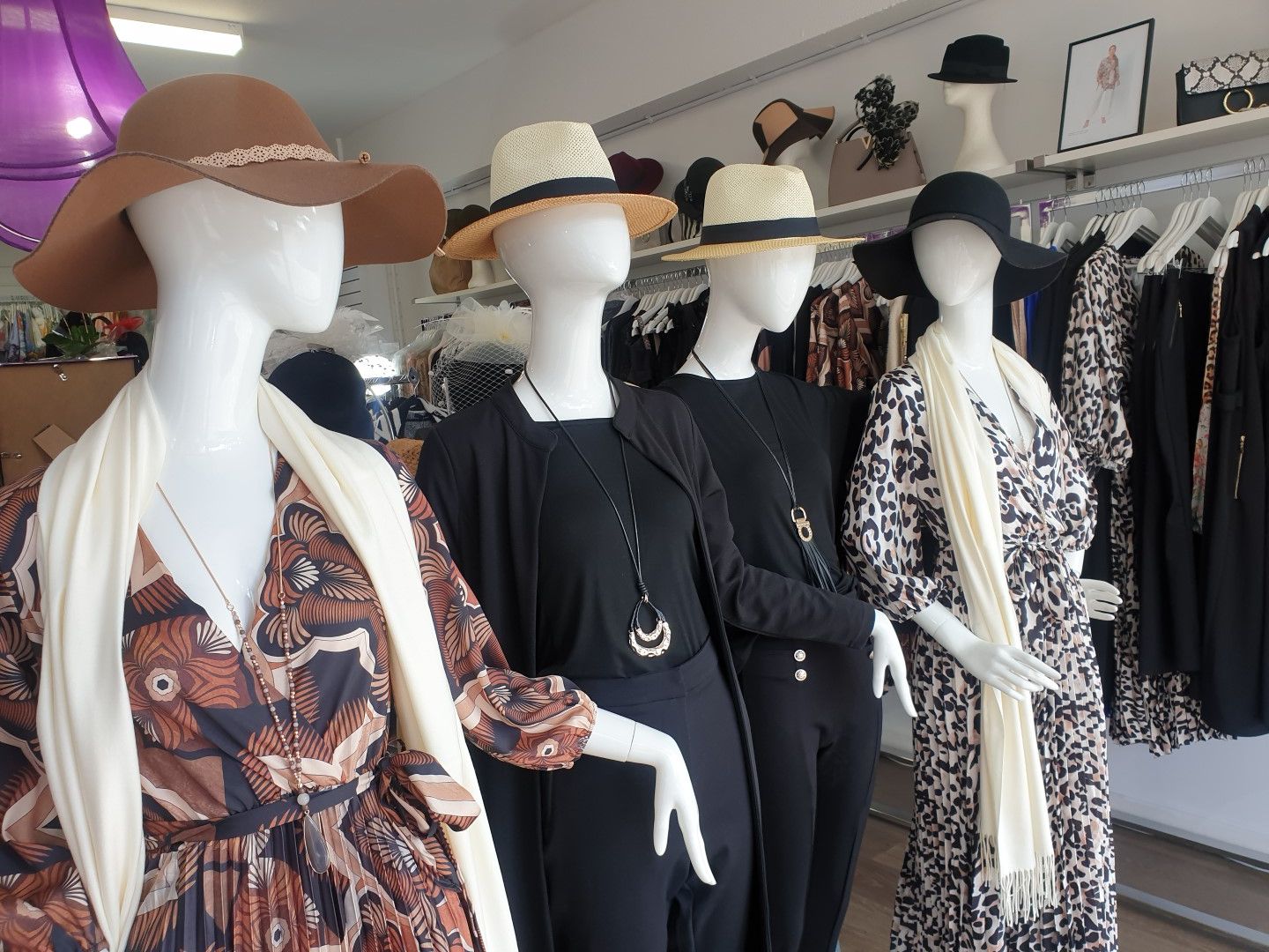 Four mannequins wearing hats, dresses, and scarves in a clothing store.