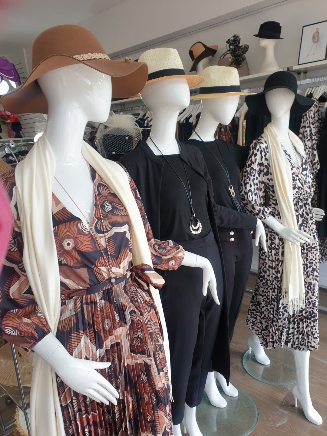 Mannequins in a boutique display dresses and hats. Beige, black, and patterned clothing.