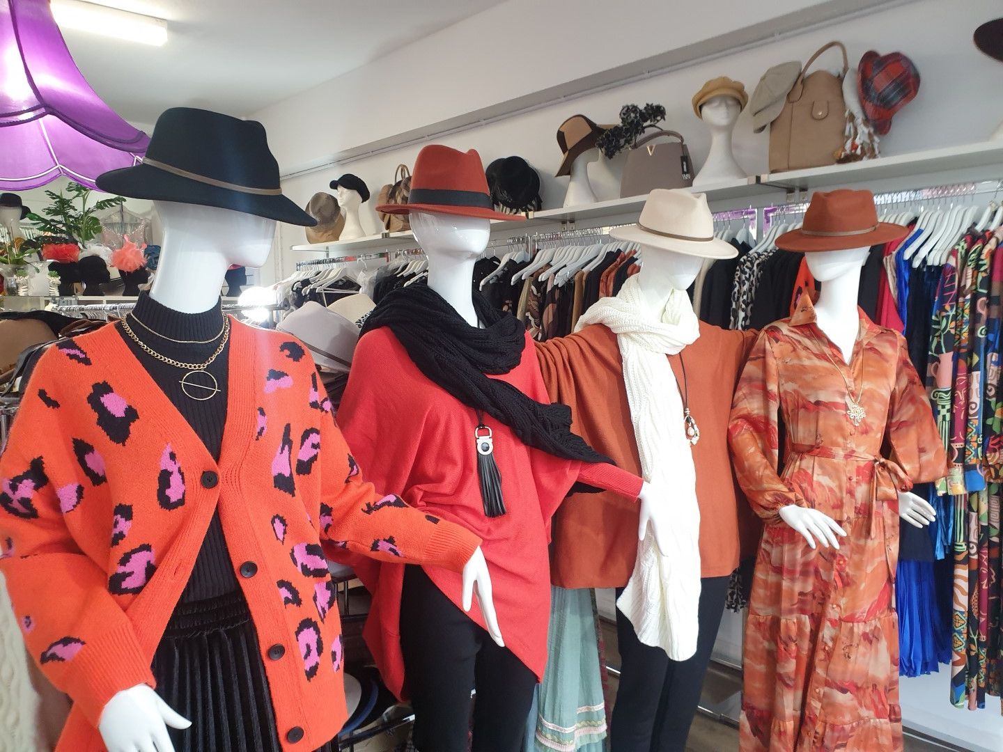 Four mannequins in a clothing store wearing hats, sweaters, and dresses in various shades of orange.